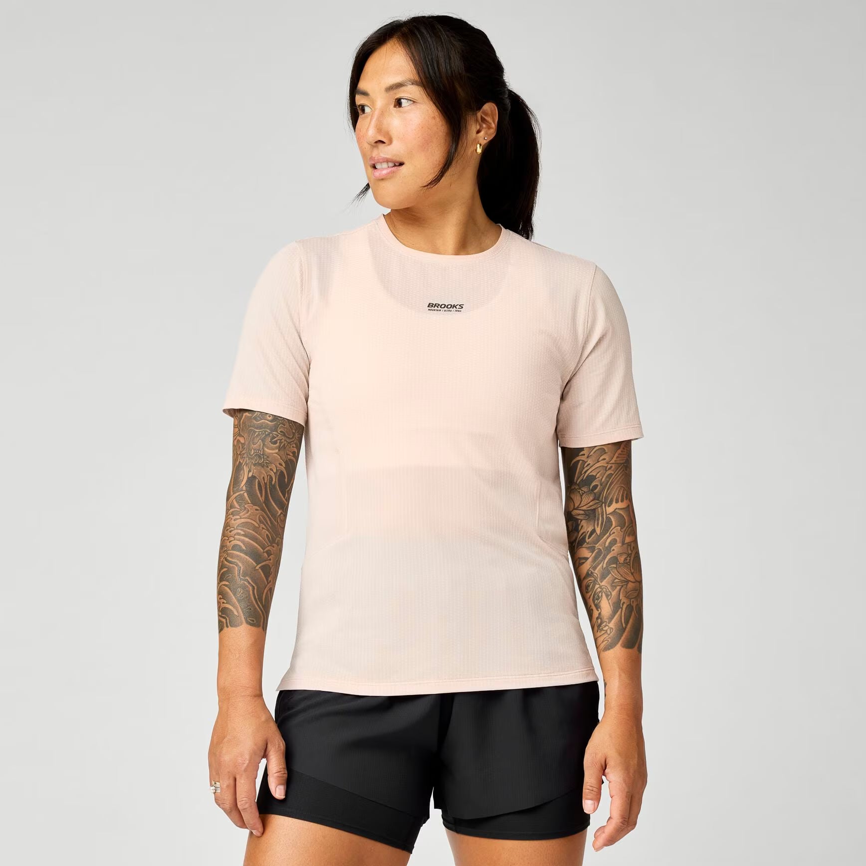 brooks womens high point short sleeve 2.0, super lightweight and breathable trail running top, light pink colour, woman wearing brooks top with grey background