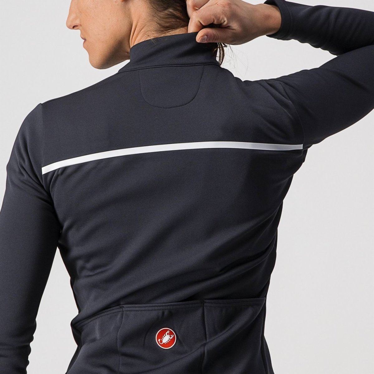 woman wearing light black castelli sinergia thermal cycling jacket, showing back reflective strip and pocket with logo