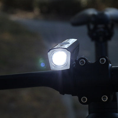 A close-up of a black Cateye AMPP 200 II bicycle headlight turned on in the dark