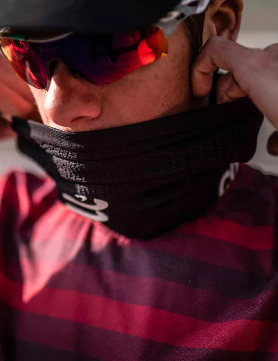 Person wearing a blackcompressport neck warmer with white text, red and black striped shirt, and reflective sunglasses.