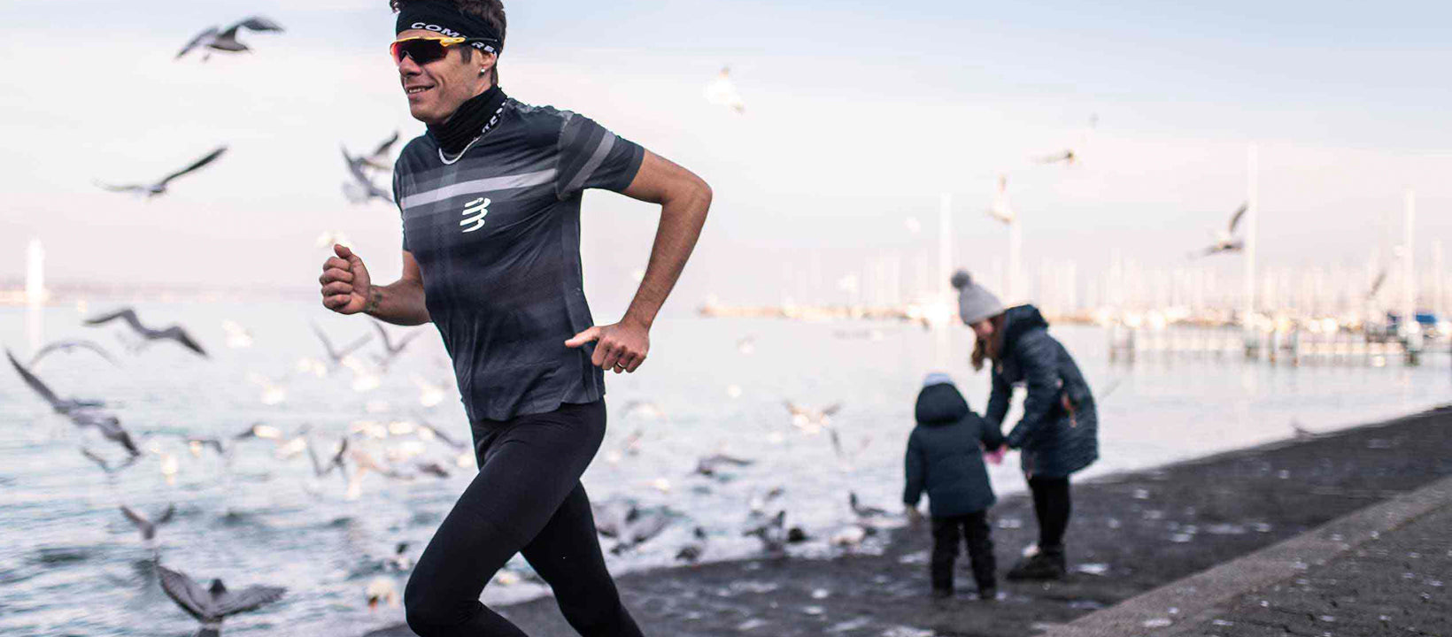 Person wearing compressport running on a path by a lake with children and seagulls in the background