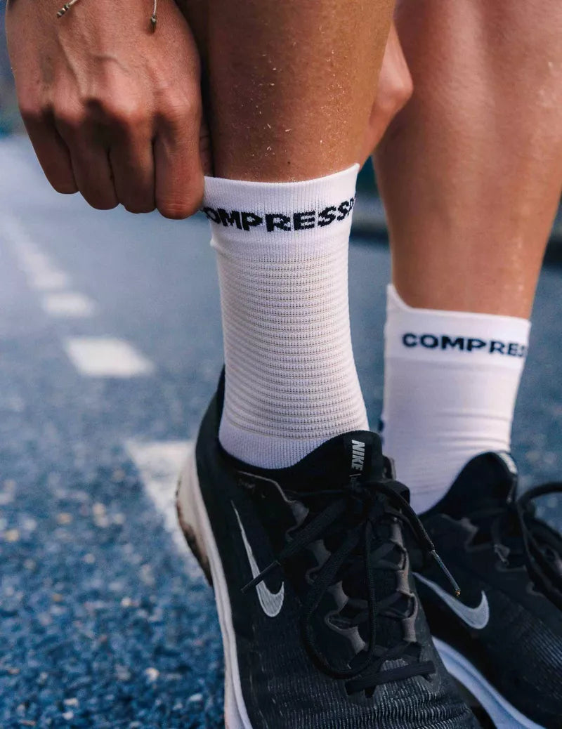 white compressport crew length road running socks on feet with black runners