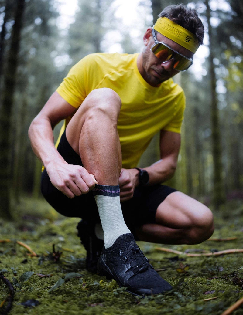 compressport pro racing trail socks, quarter length compression trail running sock, light turquoise with dark turquoise band and purple detail, man adjusting compressport sock