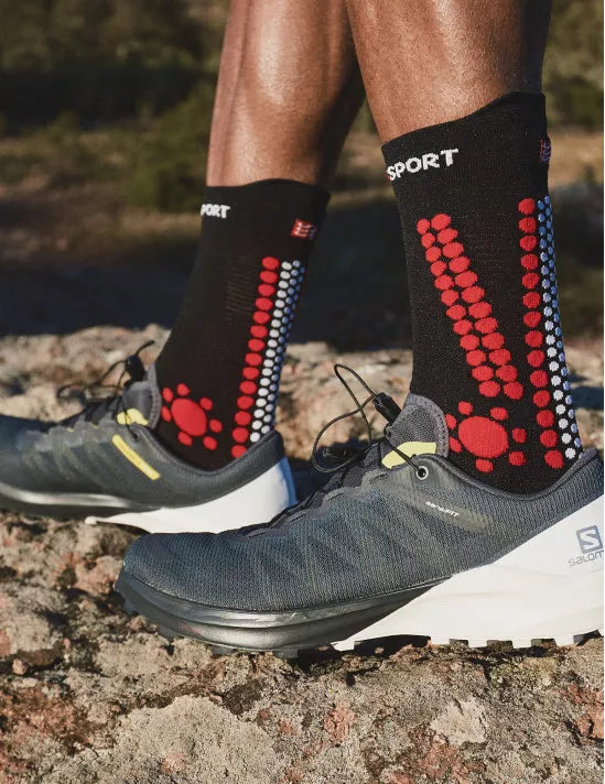 person wearing compressport pro racing trail socks, crew length compression trail running sock, red black colour with shoes
