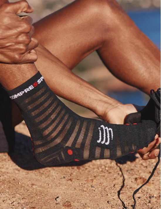 Person wearing black compression socks with visible brand logo on a blurred outdoor background
