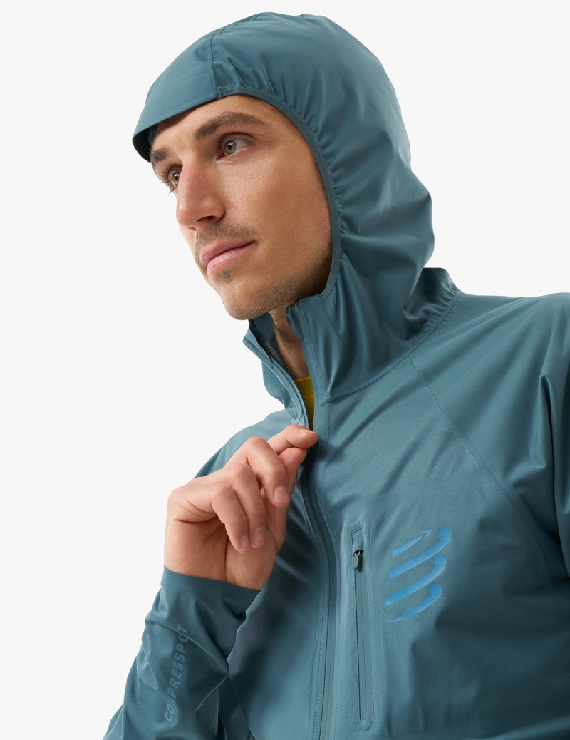 compressport tempest waterproof jacket, breathable and waterproof running jacket, deep aqua blue colour, man with hood zipped