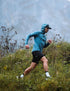 compressport tempest waterproof jacket, breathable and waterproof running jacket, deep aqua blue colour, man with hood up running in field