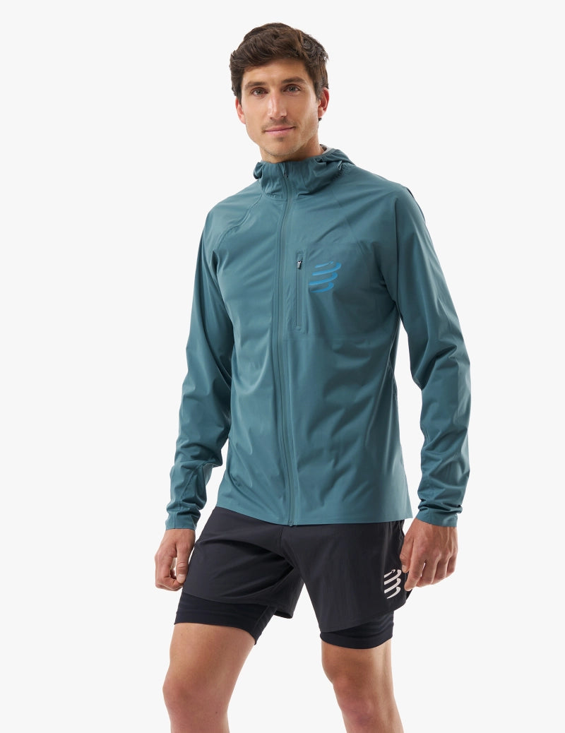 compressport tempest waterproof jacket, breathable and waterproof running jacket, deep aqua blue colour, man with jacket fully zipped