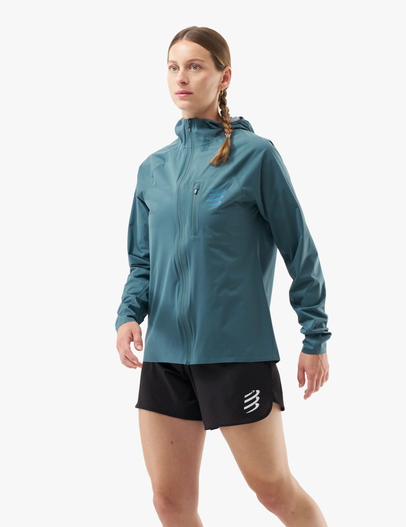 compressport tempest waterproof jacket for women, lightweight breathable and packable, dark aqua blue colour, jacket on model with hood down