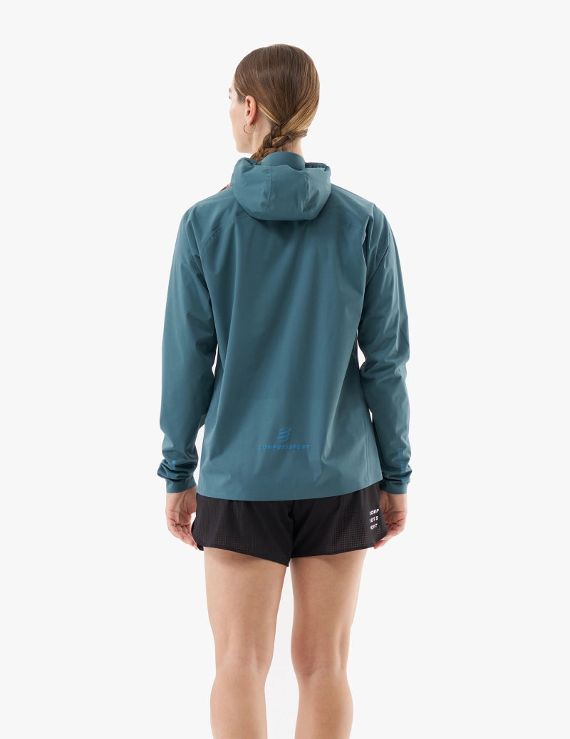 compressport tempest waterproof jacket for women, lightweight breathable and packable, dark aqua blue colour, back of jacket on model