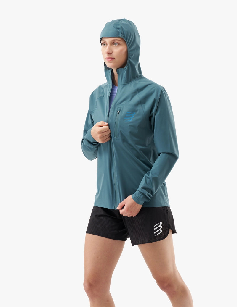 compressport tempest waterproof jacket for women, lightweight breathable and packable, dark aqua blue colour, jacket on model half zipped with hood up