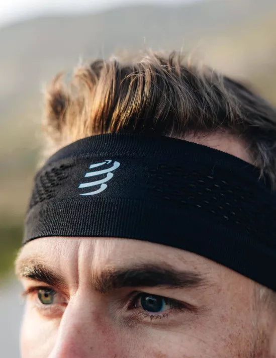 man wearing thin sports headband from compressport, in black colour with white logo
