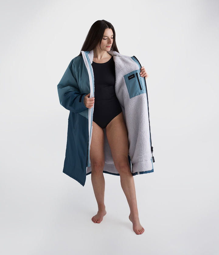 dryrobe long sleeve changing robe for all gender, light blue colour with dark blue contrast, woman wearing dryrobe zipped down, displaying light grey interior