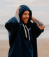dryrobe organic cotton changing robe for swimming, soft and absorbent towelling robe for all gender, navy colour, man wearing dryrobe towel on a beach background