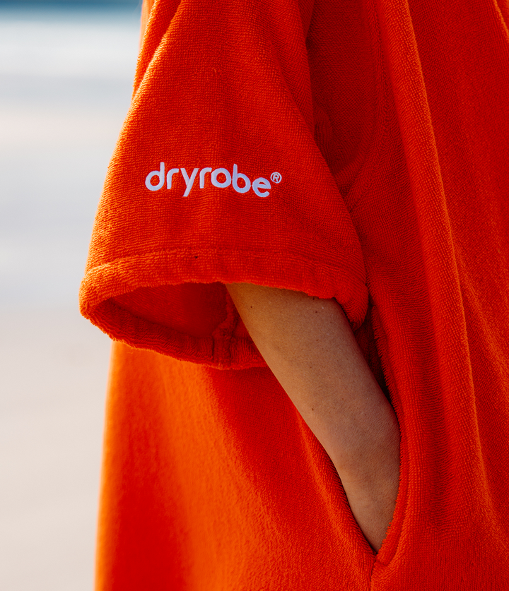dryrobe organic cotton changing robe for swimming, soft and absorbent towelling robe for all gender, orange colour, close up of woman wearing dryrobe towel 