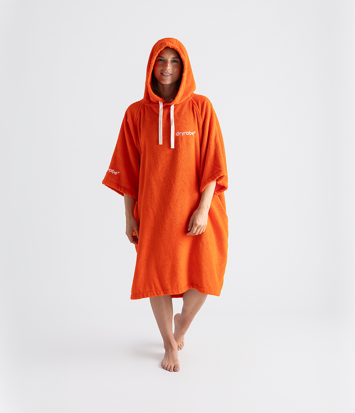 dryrobe organic cotton changing robe for swimming, soft and absorbent towelling robe for all gender, orange colour, woman wearing dryrobe towel on a white background