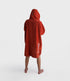 dryrobe towel robe for men and women, full zip towel robe for after swimming, dark orange colour with white sleeve caps, man wearing orange zipped up dryrobe with hood up from behind