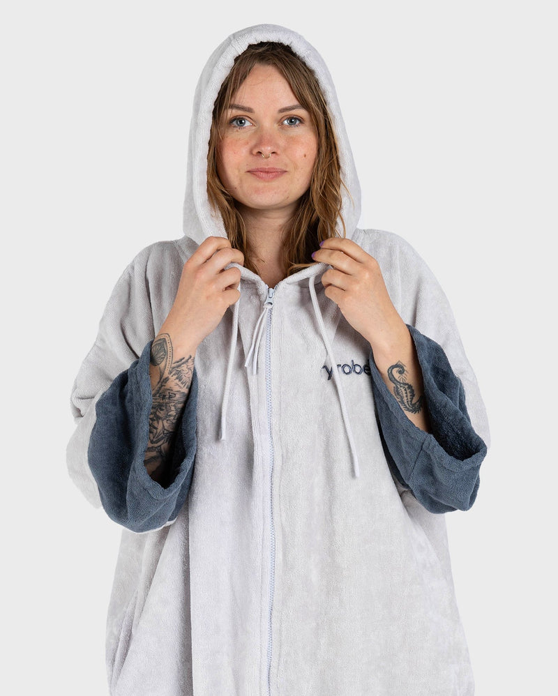 dryrobe towel robe for men and women, full zip towel robe for after swimming, light grey white colour with grey sleeve caps, woman wearing dryrobe with hood up 