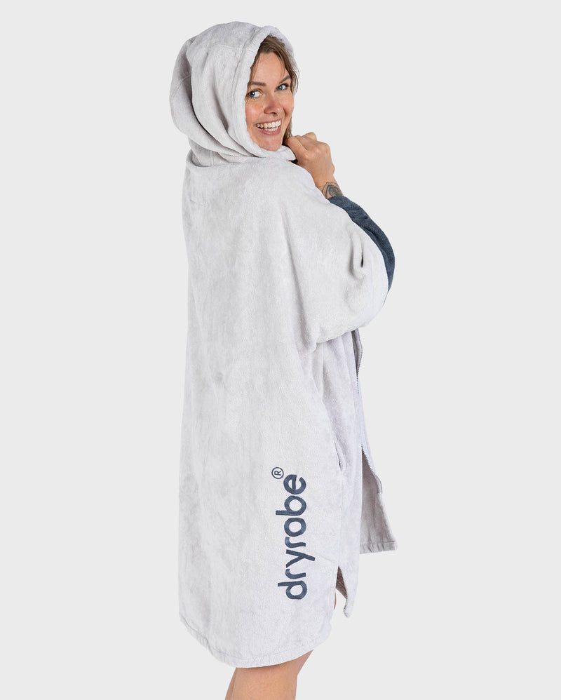dryrobe towel robe for men and women, full zip towel robe for after swimming, light grey white colour with grey sleeve caps, woman wearing dry robe side profile with dark grey logo