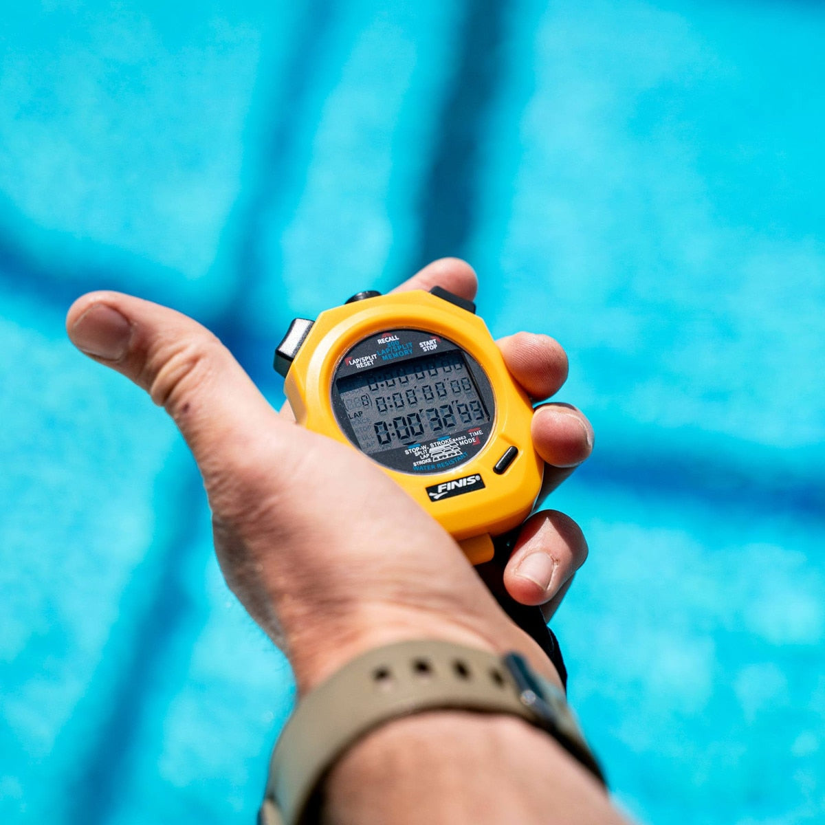 Hand holding a yellow finis stopwatch with a blue pool background