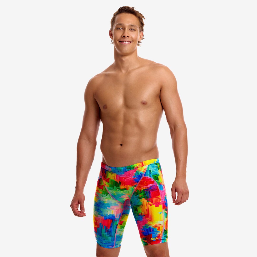 funky trunks jammers, mens tight swimming bottoms, rainbow painted pattern colour, man standing in swim shorts with white background