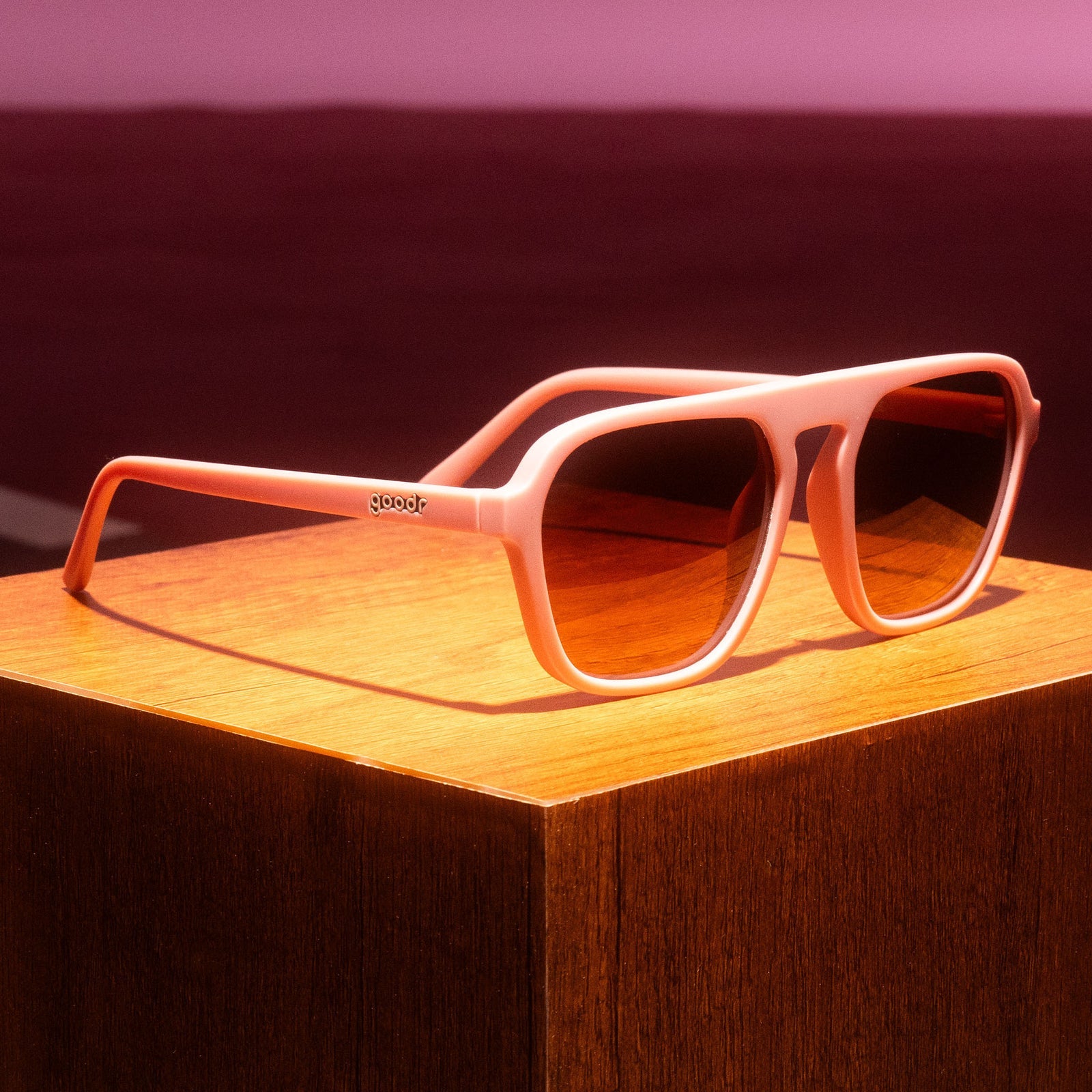 goodr glasses, threaten me with a good time, pink with brown lenses sitting on a wooden board