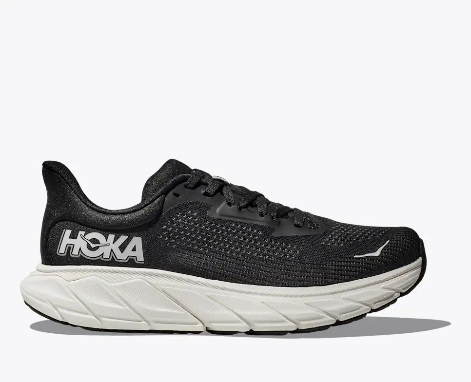 hoka arahi 7 for men, lightweight supportive running shoe, black and white colour with hite hoka logo, side profile of runner