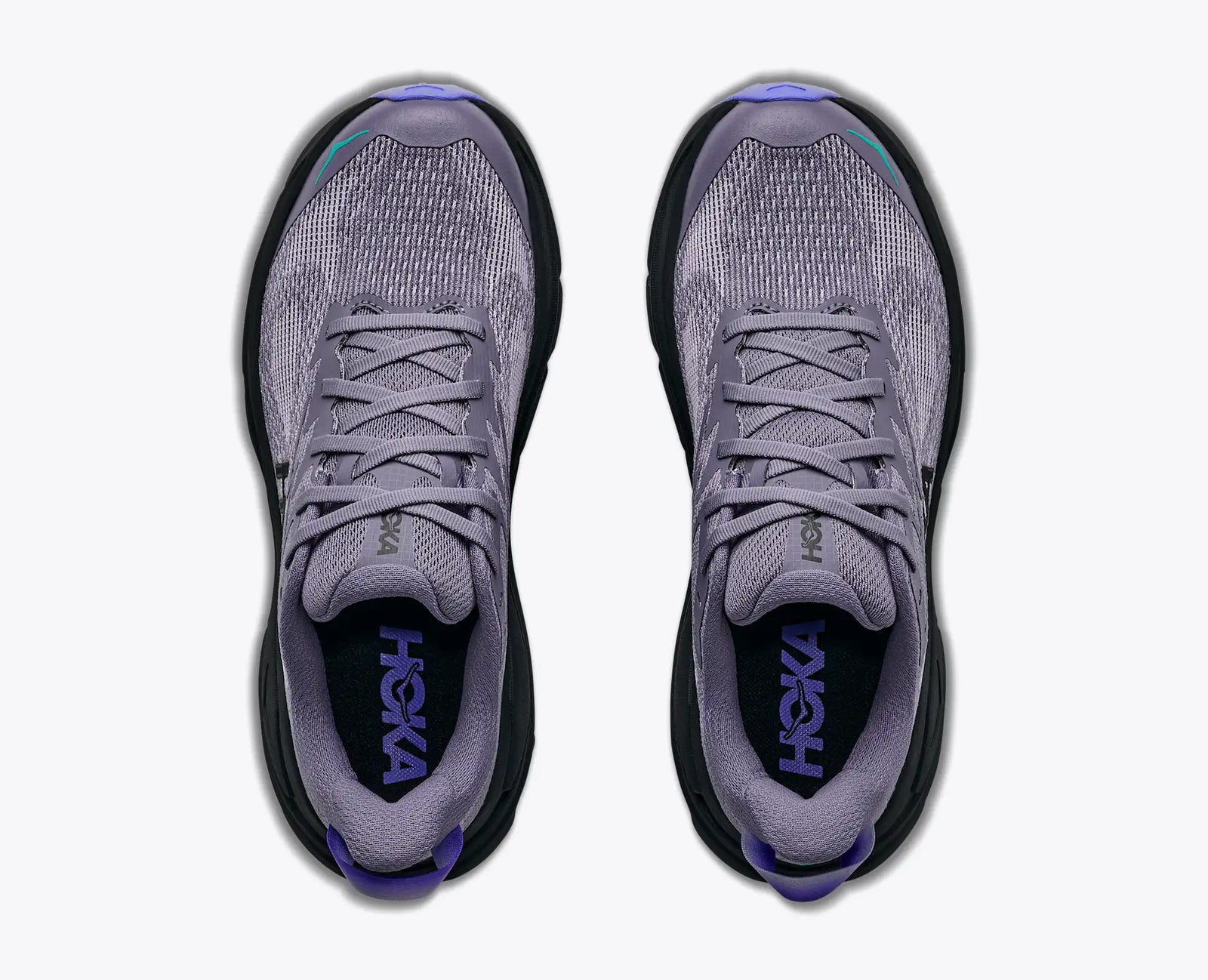 A pair of Hoka trail running shoes shown from a top-down view,light purple grey mesh upper with black soles and purple branding inside the collar.