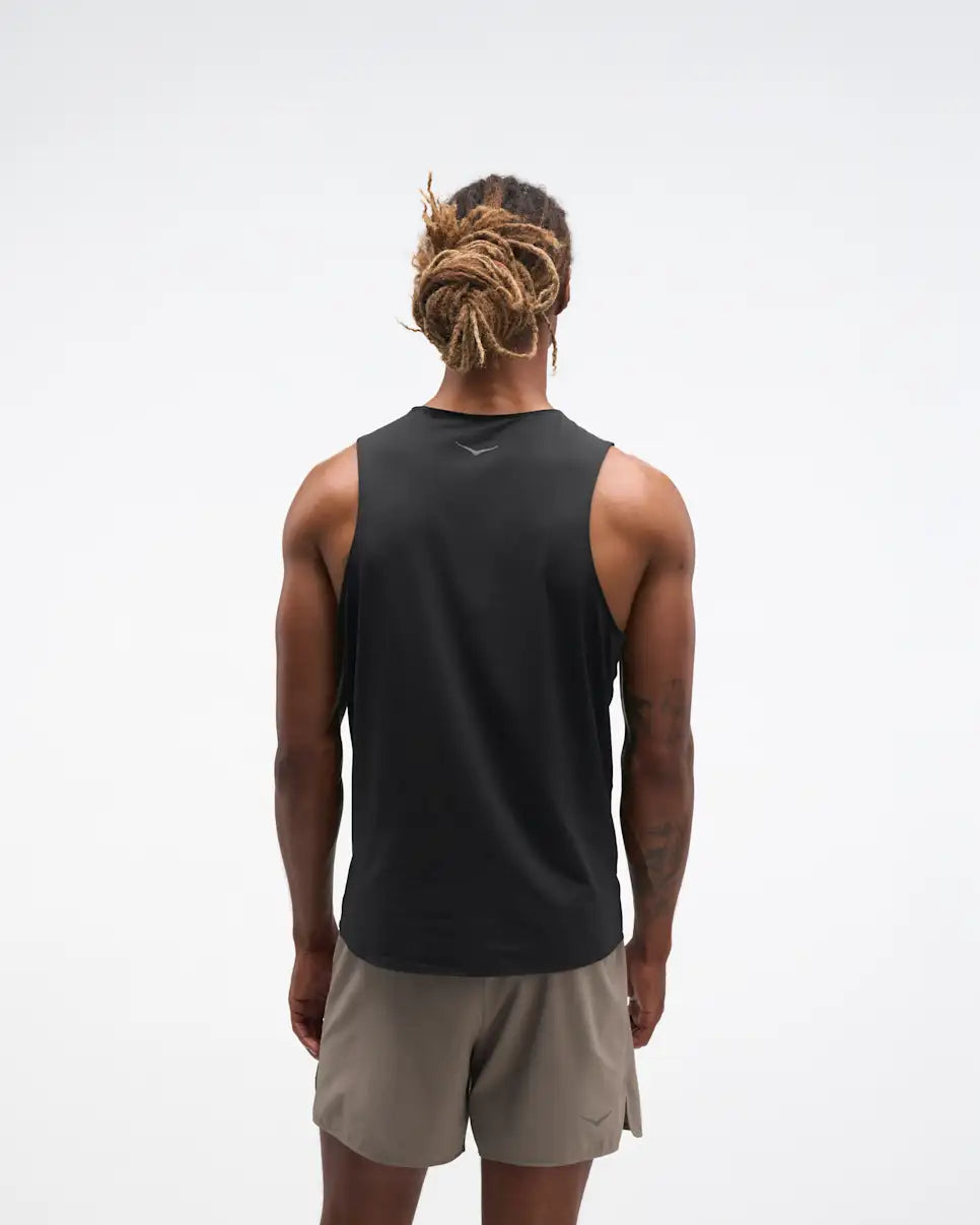 hoka everyrun tank top for men, light breathable running singlet , black colour with silver reflective HOKA logo, fback view of a man wearing hoka tank with taupe shorts