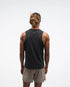 hoka everyrun tank top for men, light breathable running singlet , black colour with silver reflective HOKA logo, fback view of a man wearing hoka tank with taupe shorts