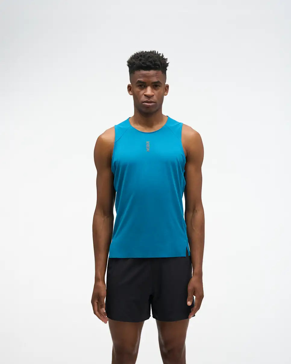 hoka everyrun tank top for men, light breathable running singlet , bright blue colour with silver reflective HOKA logo, full body profile of a man wearing hoka tank with black shorts