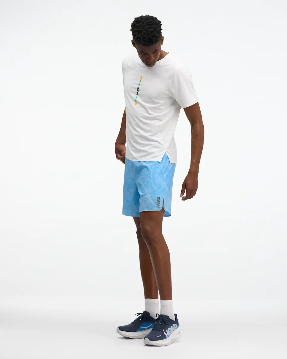 HOKA Glide 7'' Short 2-in-1, lightweight running short with inner short, light blue with white line design, side angle of man wearing shorts with white shirt and navy shoes