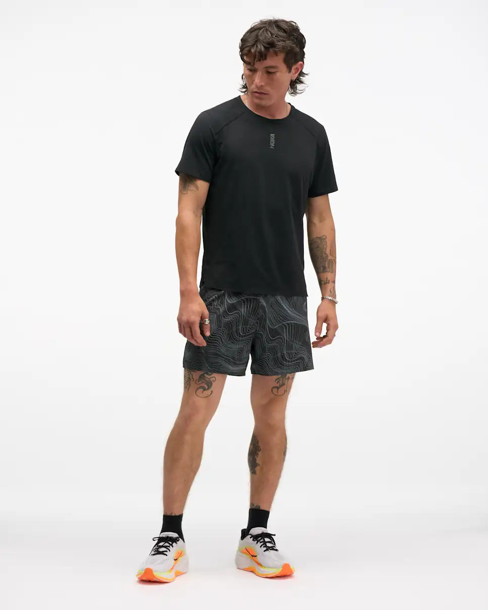 hoka 5" glide short with internal brief, black colour with white swirl pattern, full body shot of a man wearing hoka shorts with a black t-shirt on a white background