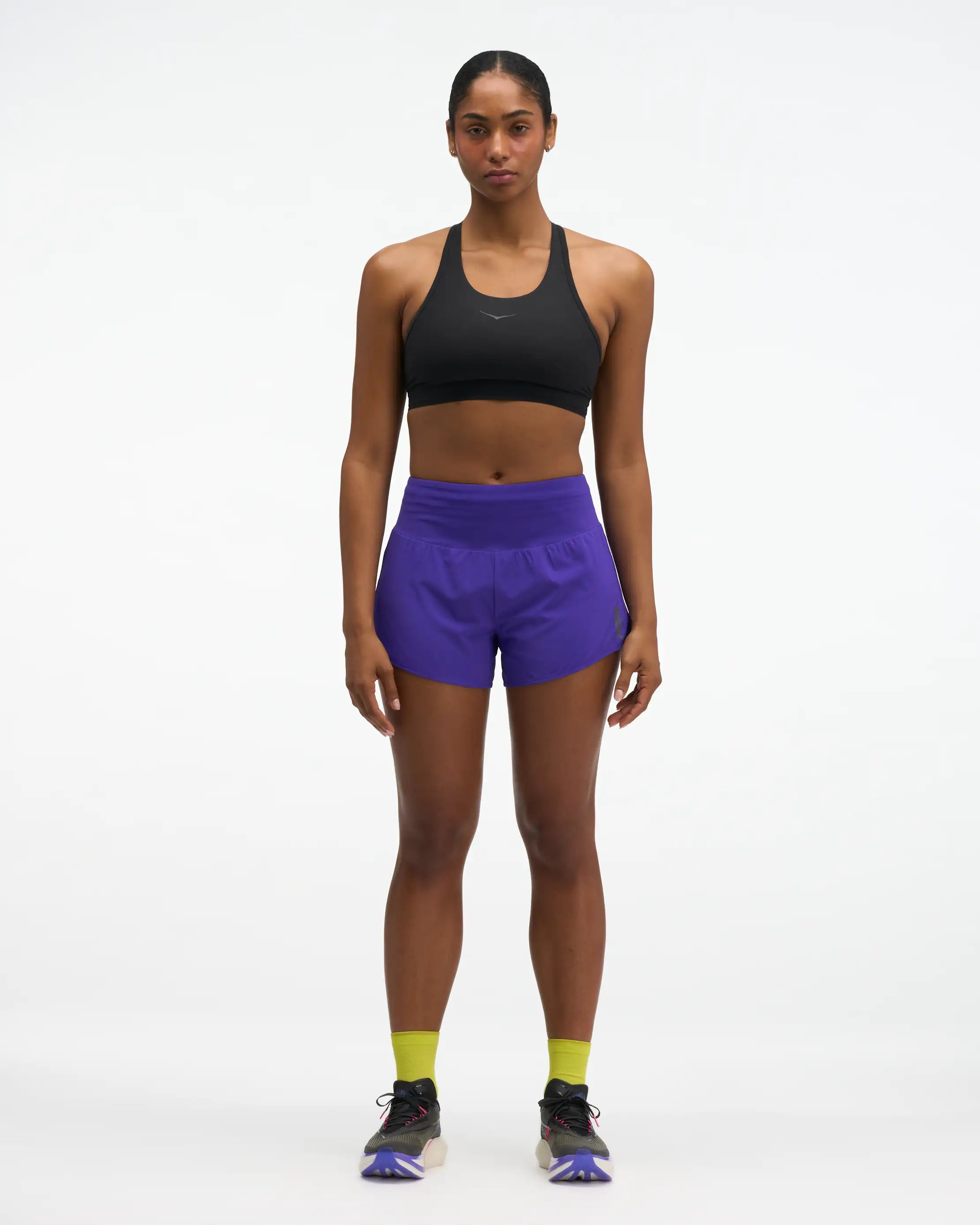 Hoka glide short mr 3.5", sweat wicking trail and road running shorts with pockets, purple shorts, woman wearing black sports bra with purple shorts with neon green socks and black runners