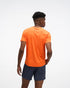 hoka everyrun short sleeve running t-shirt for men, bright orange colour with silver reflective HOKA logo, back view of a man wearing hoka tee with grey shorts on a white background