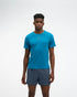 hoka everyrun short sleeve running t-shirt for men, blue colour with silver reflective HOKA logo, full body profile man wearing hoka tee with grey shorts on a white background