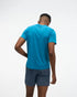 hoka everyrun short sleeve running t-shirt for men, blue colour with silver reflective HOKA logo, back view of man wearing hoka tee with grey shorts on a white background
