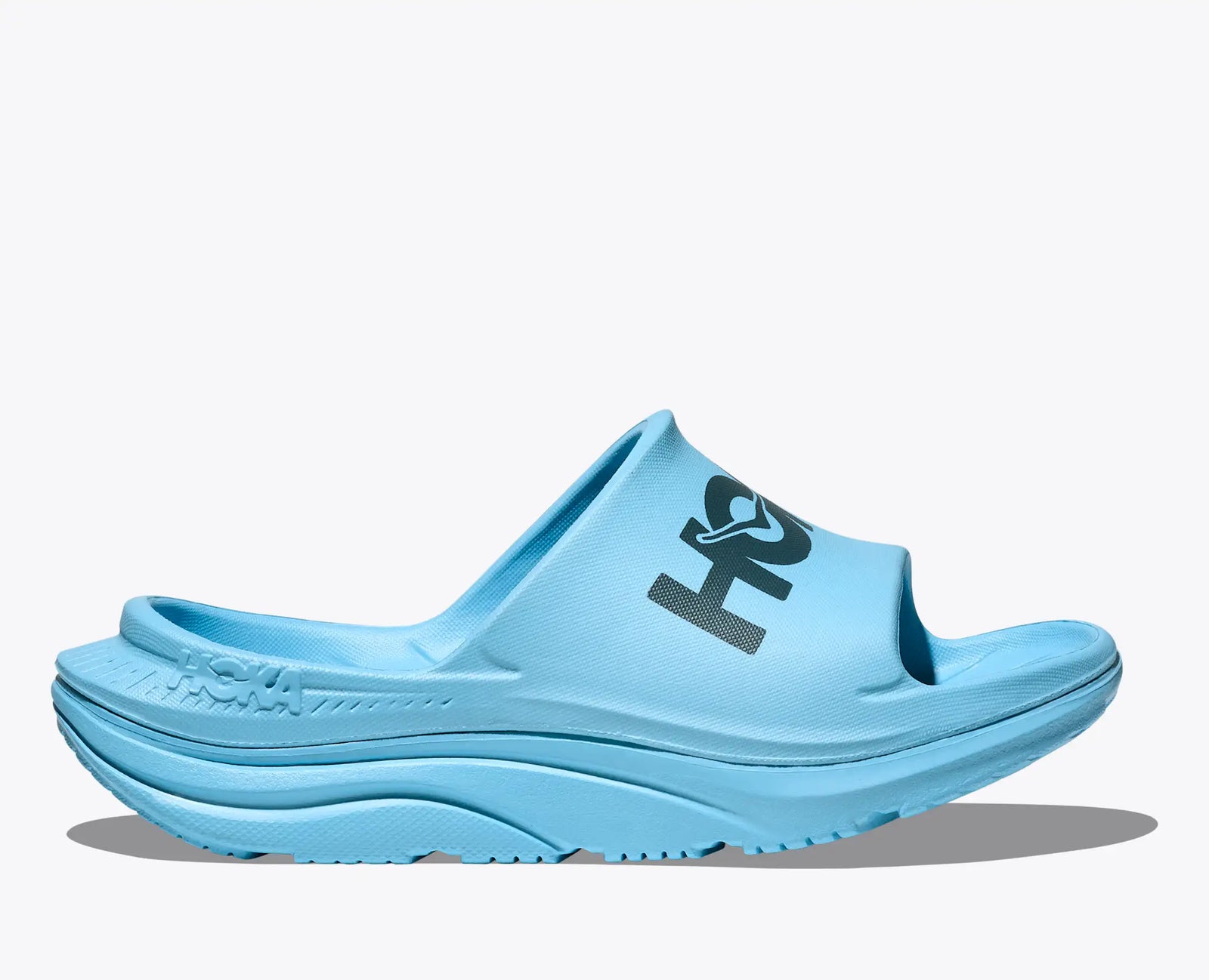 hoka ora athletic slide for men and women, cushioned slip on sandles for recovery after running, light blue colour with navy hoka logo, side profile of shoe on white background