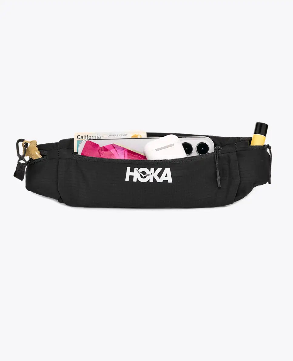 hoka running belt, running belt with zipper storage pockets, black colour with reflective logo, front of belt bag with open pocket
