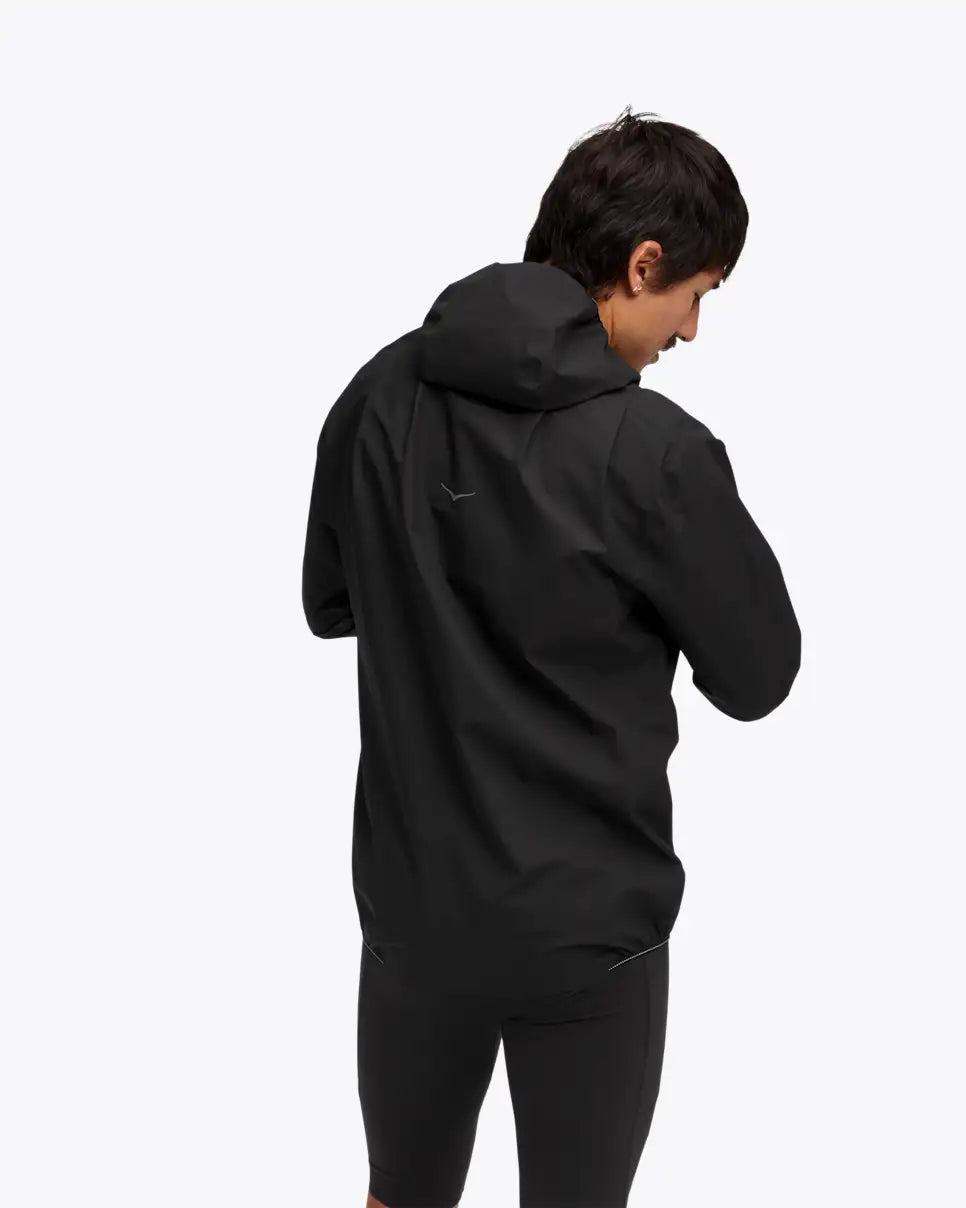 man wearing hoka skybreeze waterproof jacket, light waterproof gtx jacket for running, black colour with reflective details, view of back of jacket