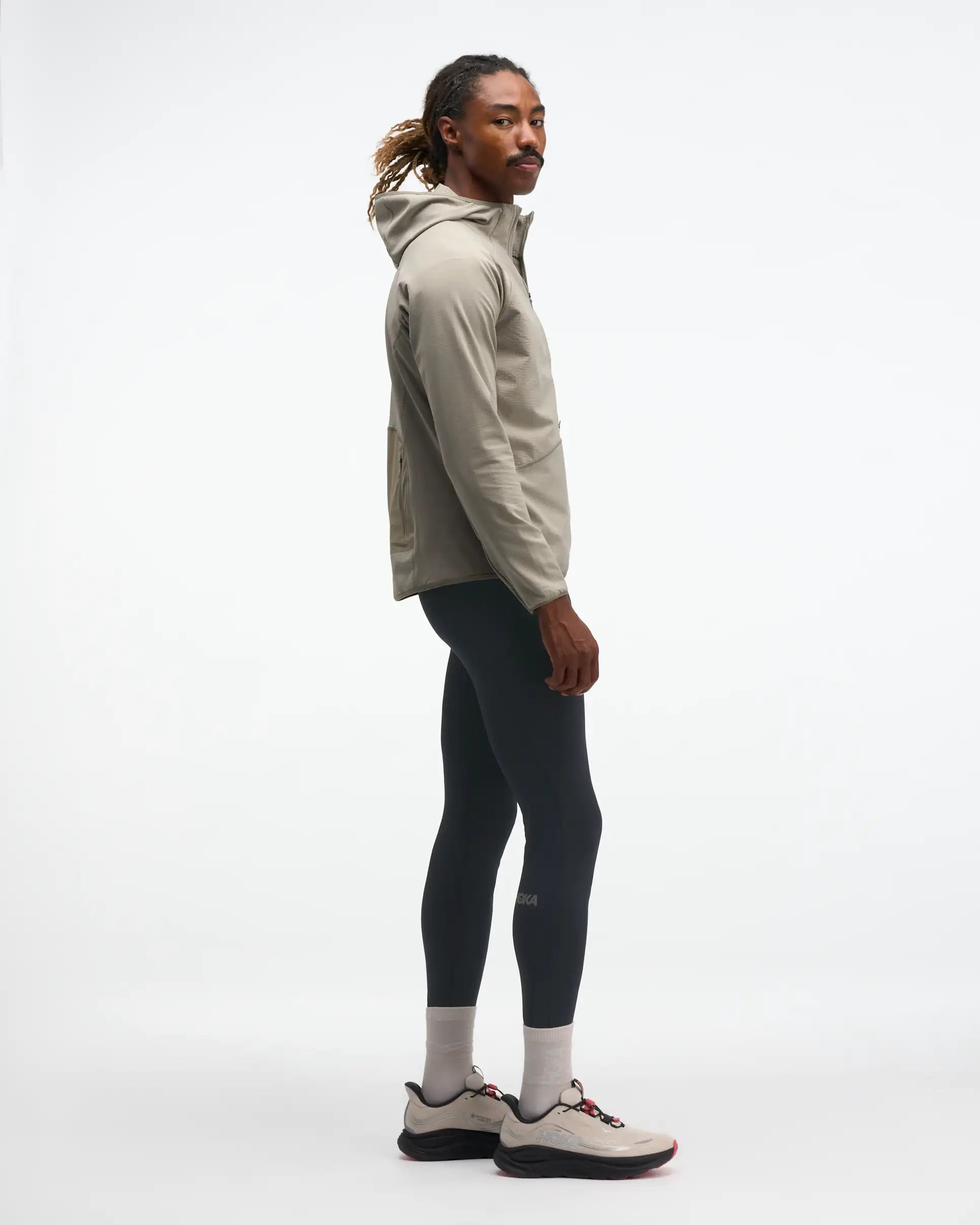 hoka men's skyglow half zip running top,  water resistant, stretchy long-sleeve pull over with a hood, light grey colour, side view of model wearing half-zip with black trousers on a white background