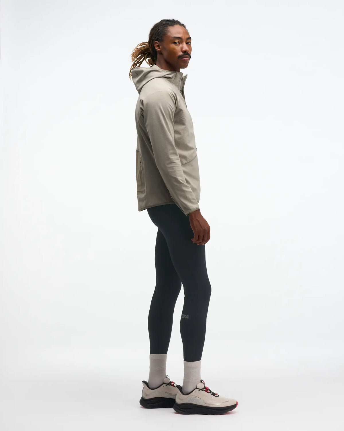 hoka men's skyglow half zip running top,  water resistant, stretchy long-sleeve pull over with a hood, light grey colour, side view of model wearing half-zip with black trousers on a white background