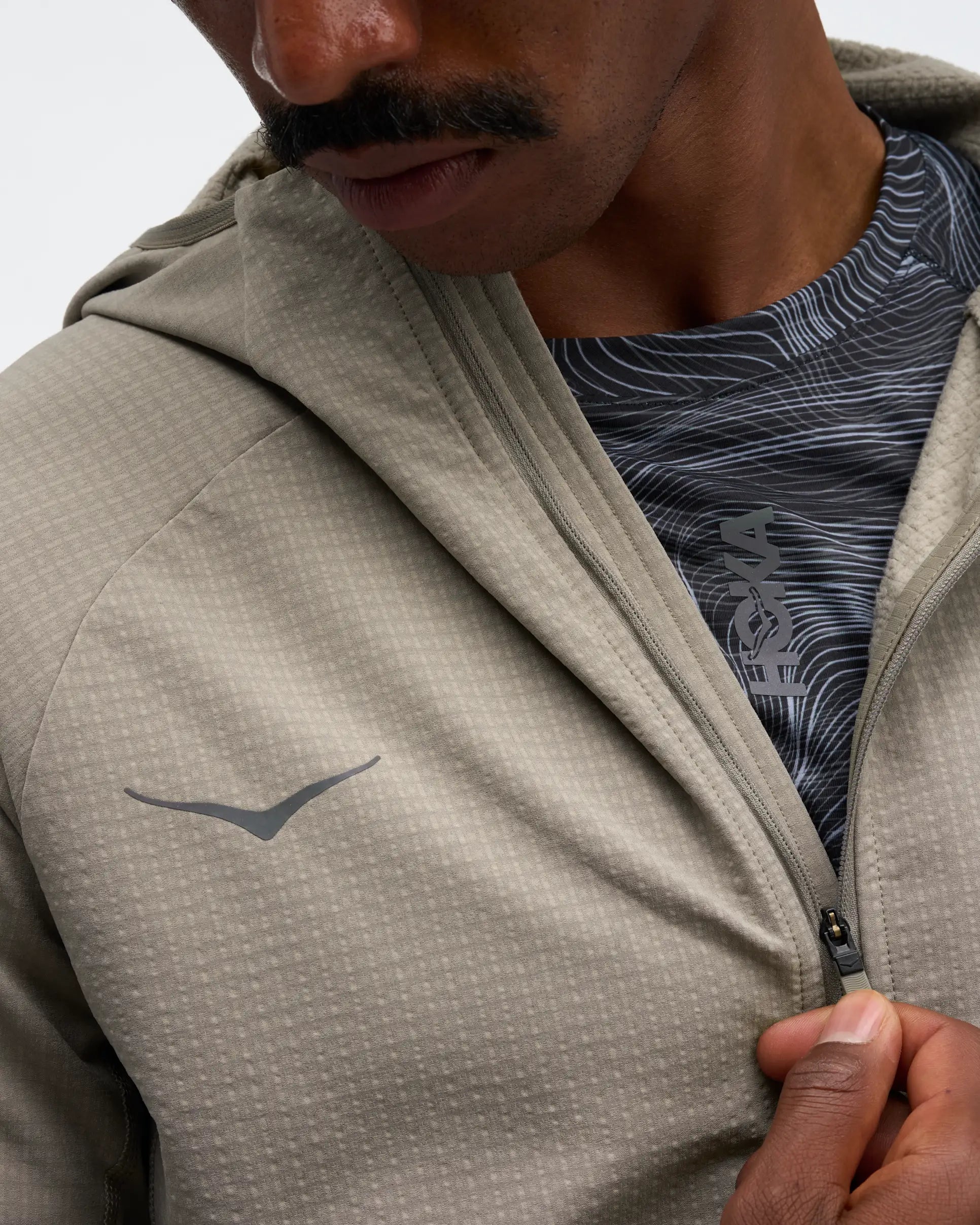 hoka men's skyglow half zip running top,  water resistant, stretchy long-sleeve pull over with a hood, light grey colour, close up view of model wearing half-zip 