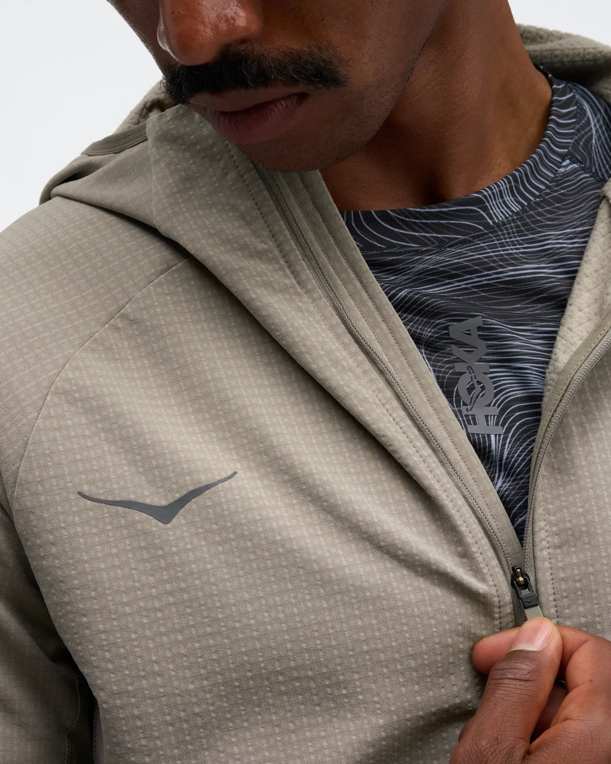 hoka men's skyglow half zip running top,  water resistant, stretchy long-sleeve pull over with a hood, light grey colour, close up view of model wearing half-zip 