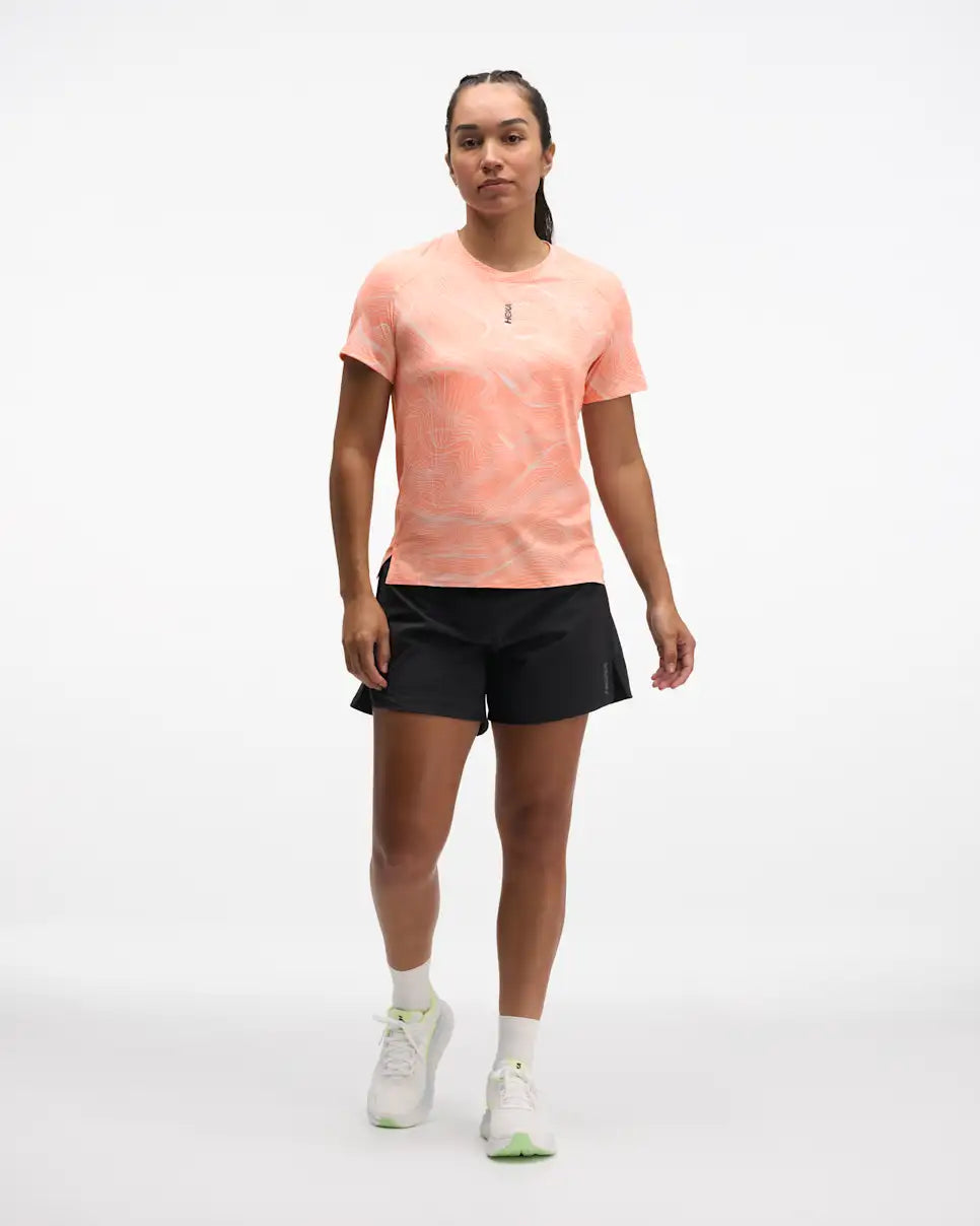 hoka everyrun short sleeve running t-shirt for women, peach colour with silver reflective logo, front view of woman wearing hoka tee with black shorts on a white background