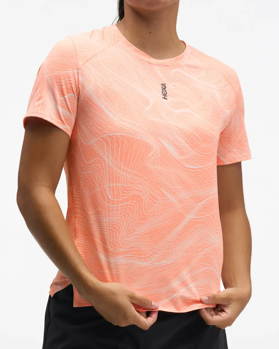 hoka everyrun short sleeve running t-shirt for women, peach colour with silver reflective logo, front view of woman wearing hoka tee with black shorts on a white background