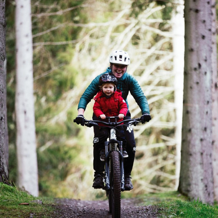 Kids Ride Shotgun Child Bike Seat + Handlebars Combo, woman riding bike with child on seat through forest with helmets