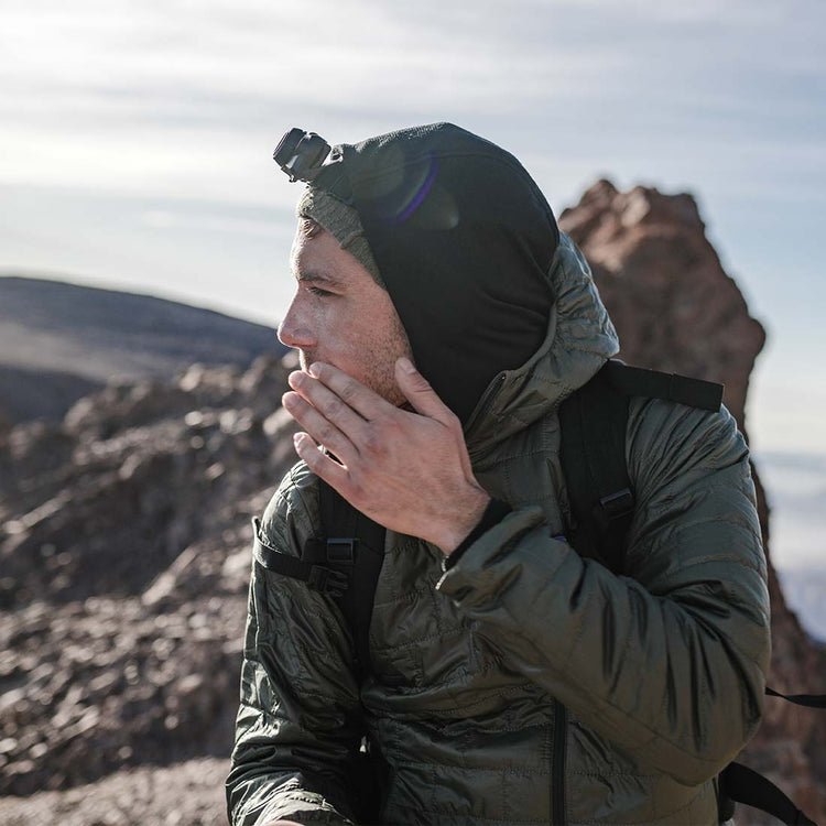 Person wearing a hooded jacket applying sun cream in a desert landscape