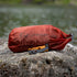 lifeventure ultralight dry bag, 5 litre capacity, waterproof and durable storage bag, red rust colour, displayed on a rock with a body of water in the background