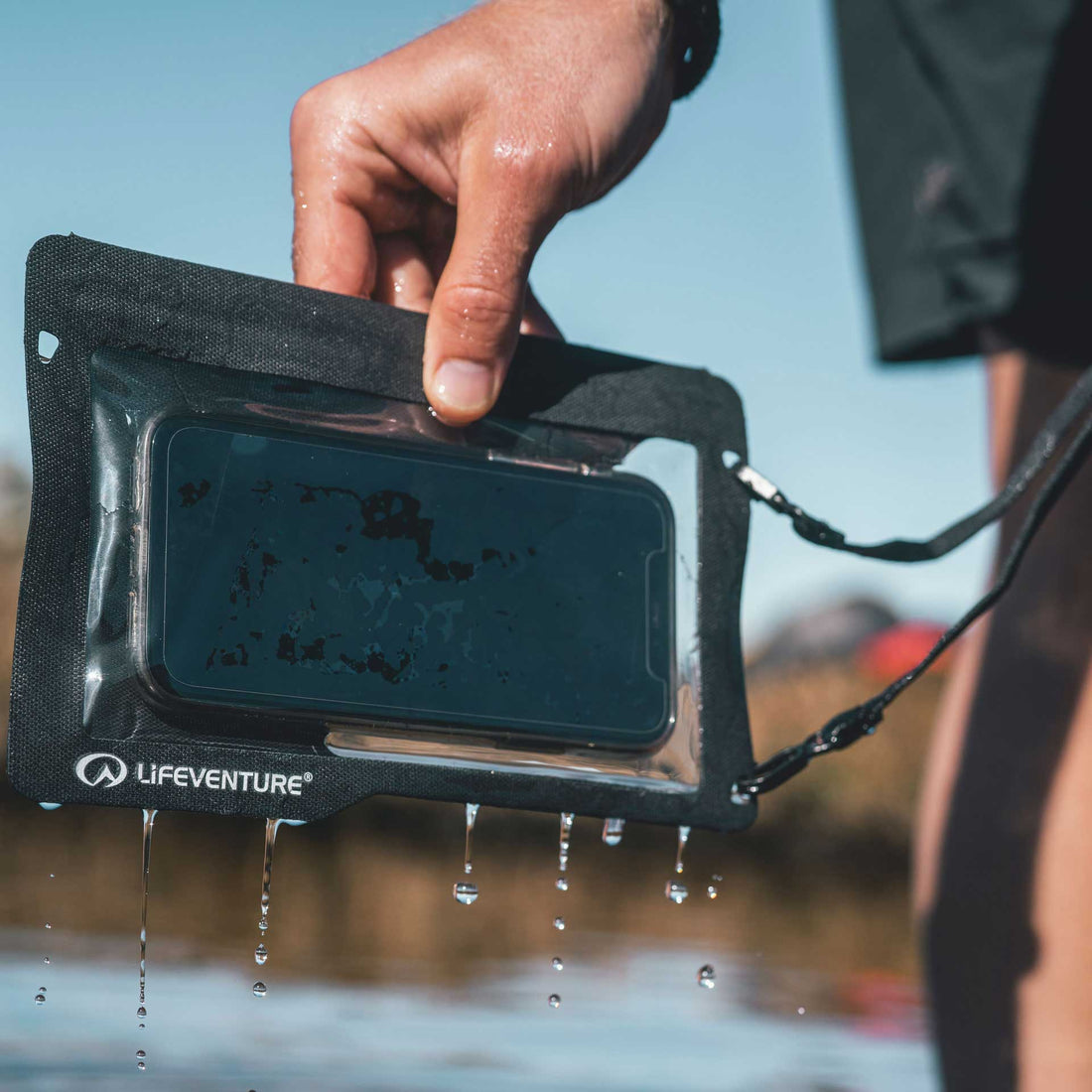 Person holding a waterproof phone case with Lifeventure branding, outdoors.